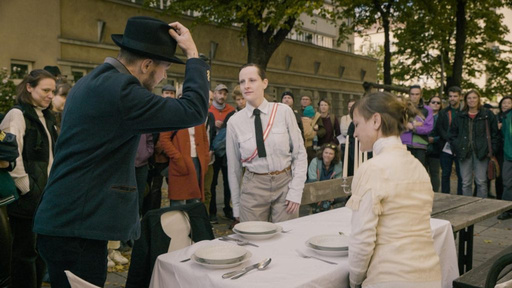 Schauspieler*innen an einem Tisch vor Publikum