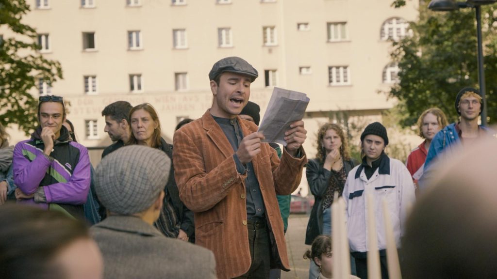 Ein Schauspieler liest etwas von einem Stück Papier vor
