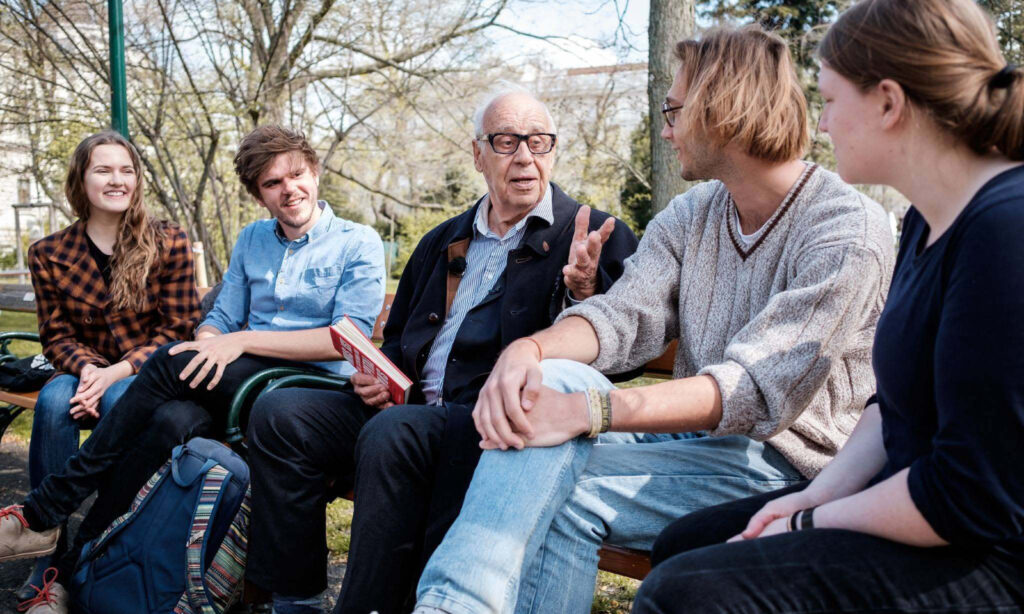 Das Bild zeigt Jean Ziegler mit Vertreter*innen von Fridays for Future Vienna, gemeinsam auf einer Parkbank sitzend und sich unterhaltend.