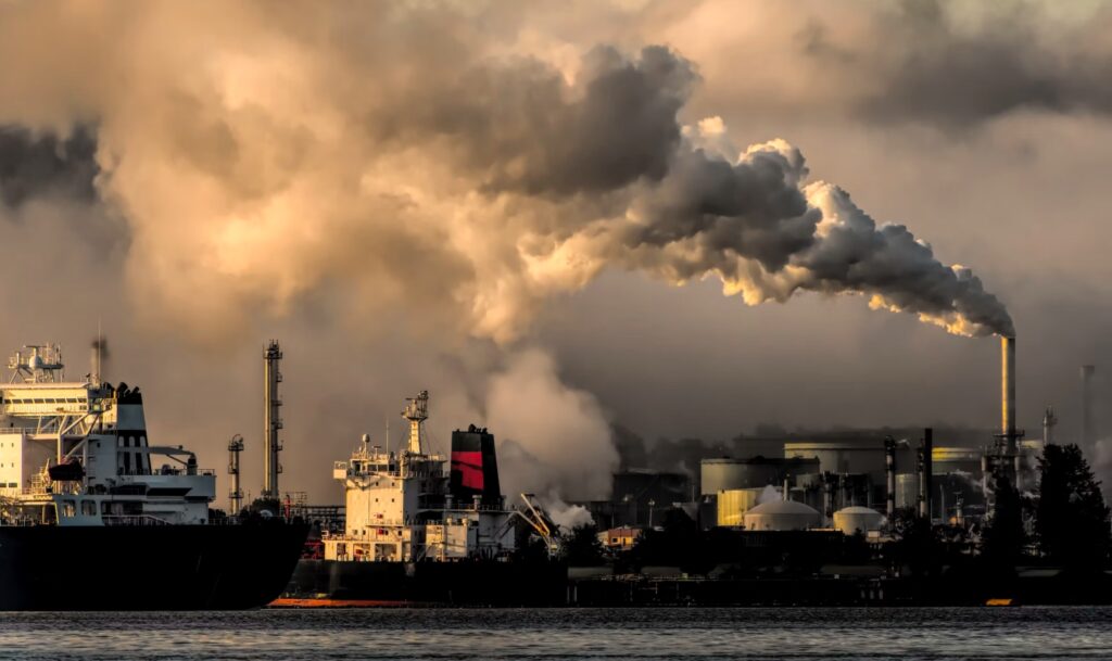 Das Bild zeigt eine Industrieanlage mit rauchenden Schornsteinen bei Sonnenuntergang.